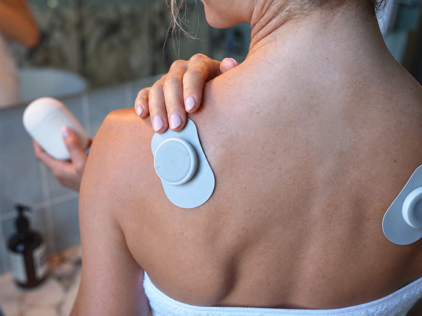 Woman applying the Calvonic TENS Pod to her shoulder after a shower